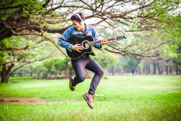 istock Asian young men jump in nature playing guitar 933458586