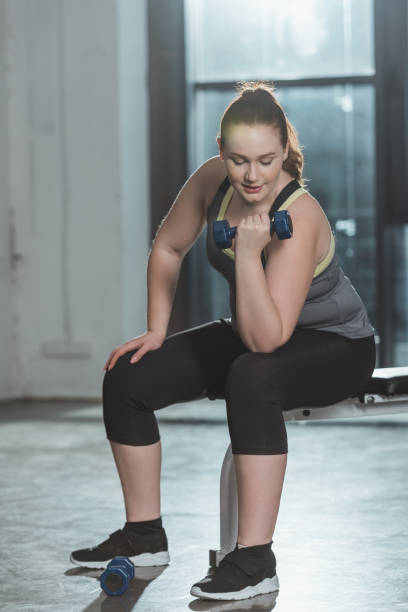 istock Overweight girl training with dumbbell in gym 933475256