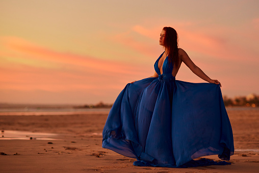 attractive woman in electric blue dress enjoying sunset silence, holding dress and relaxing.