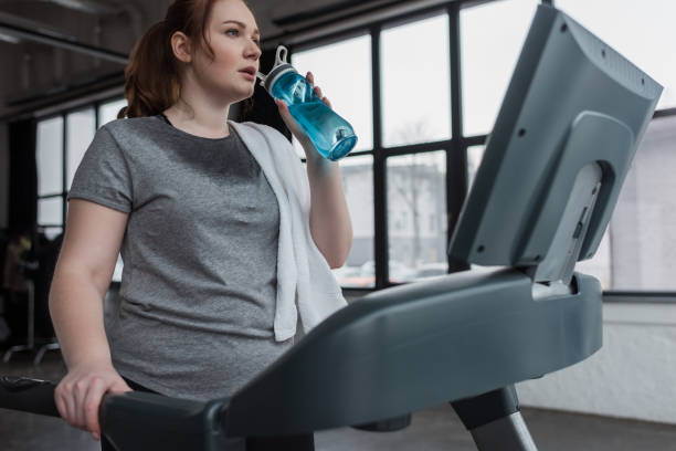 istock Curvy girl drinking from water bottle while running on treadmill in gym 933475864