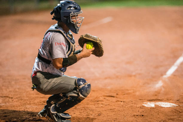 Softball Catcher Kneeling and Holding the Ball Softball Catcher Kneeling and Holding the Ball catchers mask stock pictures, royalty-free photos & images