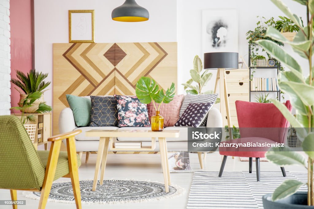 Patterned cozy living room Patterned pillows on sofa next to red armchair in cozy living room interior with wooden furniture Cushion Stock Photo