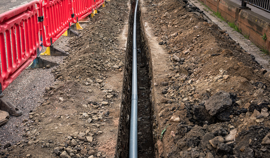 A new pipe being installed under the street, with a long trench dug through the road surface.