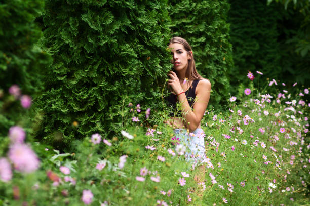 fashion model standing in flowers leaning against green tree looking at camera