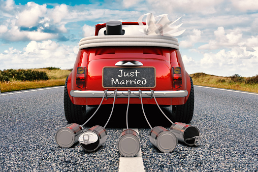A newlywed couple is driving a retro car with just married sign and cans rear view 3D rendering