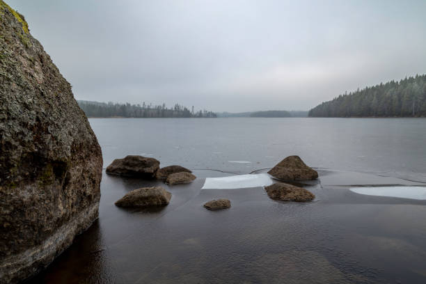 istock ice and stones at a small lake with forest all around 933603072