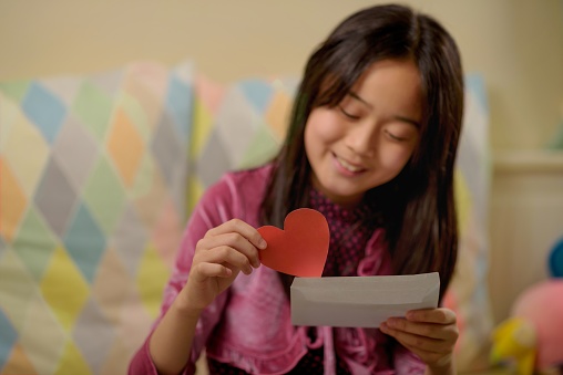 Asian girl putting a heart shaped paper into a envelope