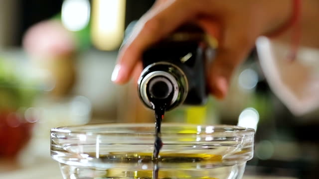 Sous chef pouring balsamic vinegar in olive oil salad dressing, healthy food