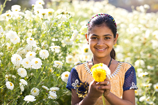 Happy Indian girl holding daisy flowers in field