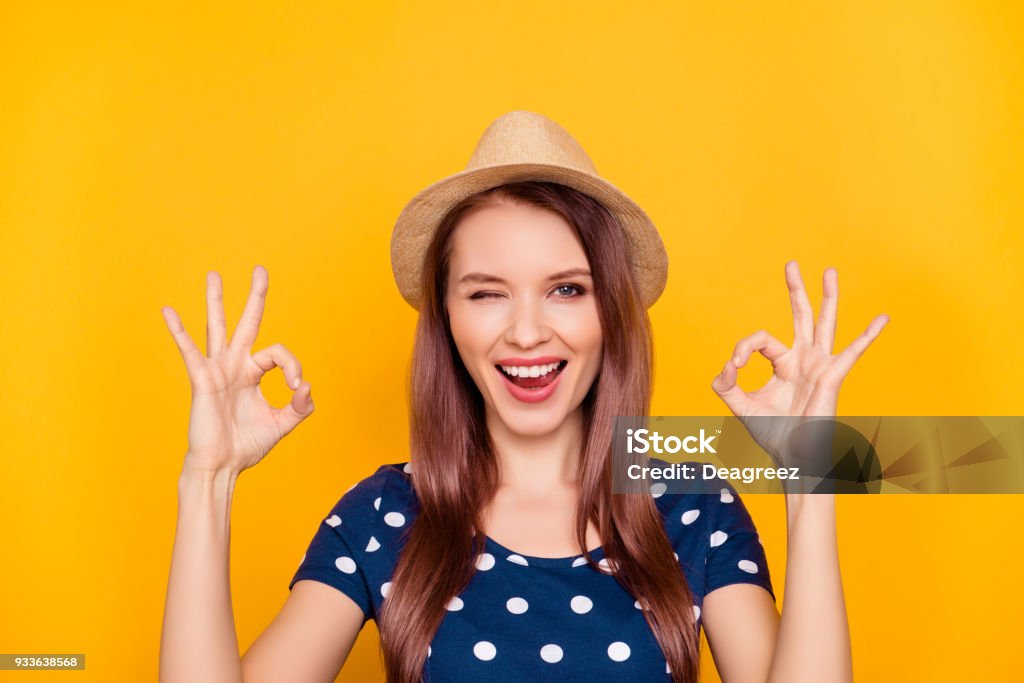 Portrait of sexy, charming, pretty, nice, trendy, laughing girl in polka-dot t-shirt showing two ok sign with fingers, blinking with eye at camera, isolated on yellow background OK Sign Stock Photo