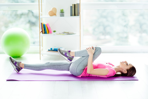 Profile side view photo of purposeful enduring with beautiful figure slender charming teenage girl doing exercises for stretching legs limbering up before doing sport lying on purple mat white light