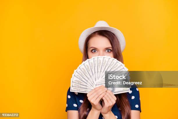 Portrait Of Pretty Charming Girl Holding In Hand A Lot Of Money Close With Fan Half Face Looking Out With Eyes Having White Hat On Head Isolated On Yellow Background Stock Photo - Download Image Now
