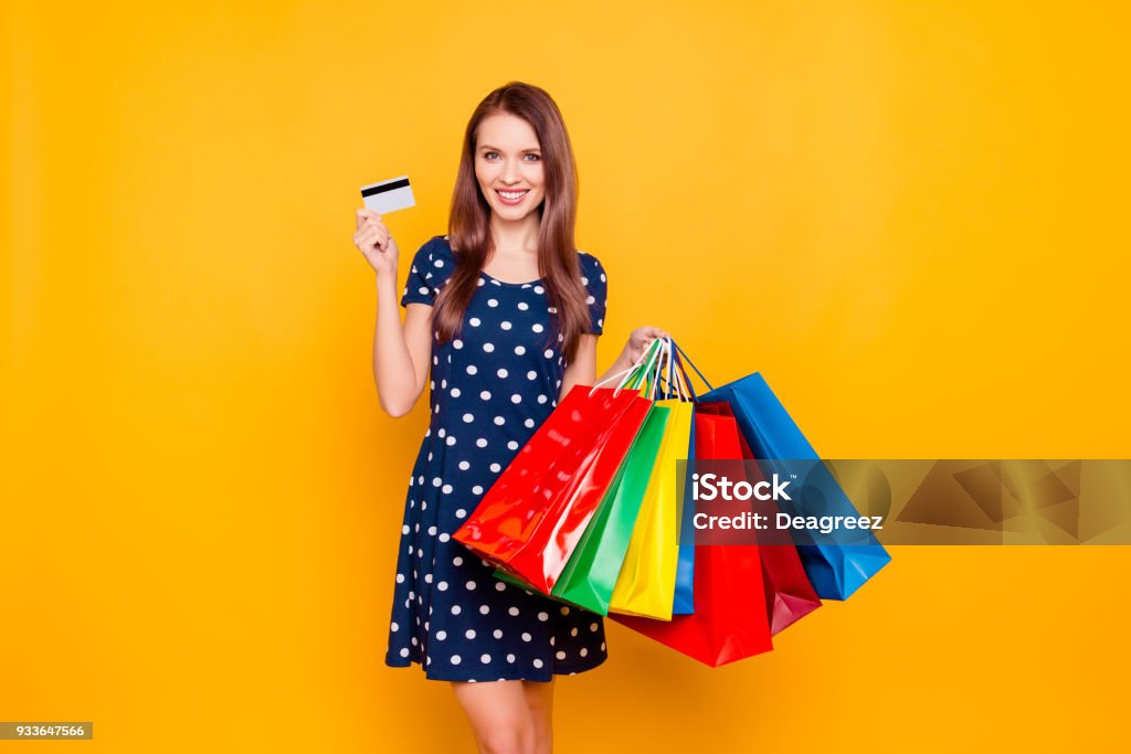 Charmant ziemlich attraktives sexy Mädchen mit Kreditkarte und halten viele bunte Pakete in der Hand, ist es bequem, Bankkarte zum Einkaufen zu verwenden, über gelben Hintergrund stehen - Lizenzfrei Einkaufstasche Stock-Foto