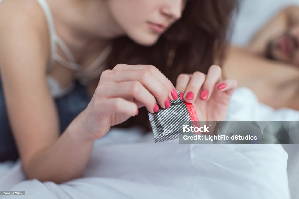 cropped shot of woman opening condom on bed Condom Stock Photo