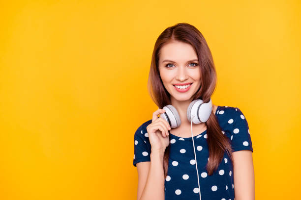 portrait avec l’espace de la copie d’une fille charmante, moderne, jolie, gentil, en t-shirt pois avoir un casque sur son cou, tenant la main sur le casque, regardant la caméra, isolé sur fond jaune - polka dot audio photos et images de collection