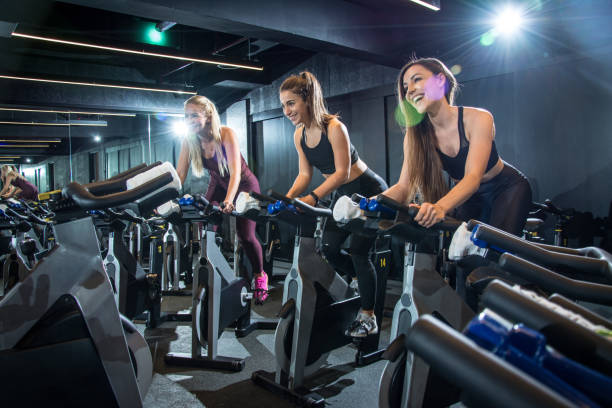 donne sportive felici in sella a cyclette in classe ciclistica in palestra. - spinning foto e immagini stock