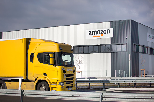 Facade of new logistics center of amazon in Raunheim-Moenchhof, Germany. Amazon (Amazon.com, Inc.) is an American electronic commerce and cloud computing company and the largest Internet retailer in the world as measured by revenue and market capitalization. In the foreground a passing freight truck