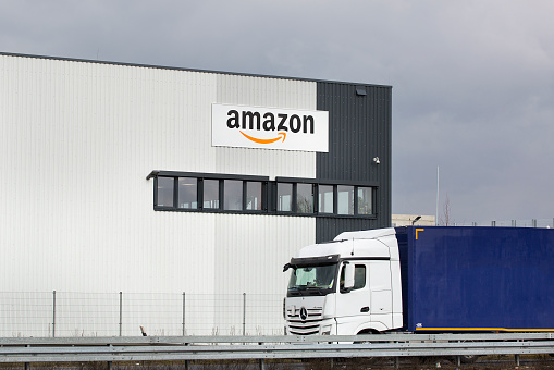 Facade of new logistics center of amazon in Raunheim-Moenchhof, Germany. Amazon (Amazon.com, Inc.) is an American electronic commerce and cloud computing company and the largest Internet retailer in the world as measured by revenue and market capitalization. In the foreground a passing freight truck