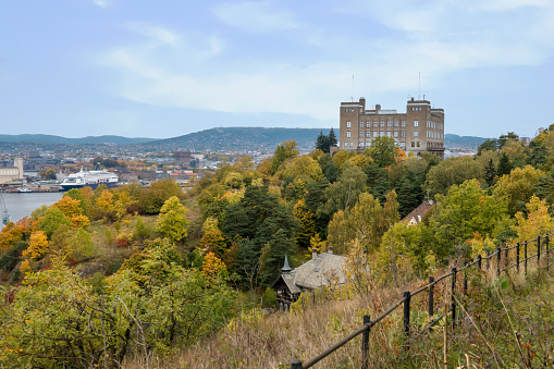 Cityscape of Oslo city with autumn forest in foreground with a brown square building, Oslo, Norway