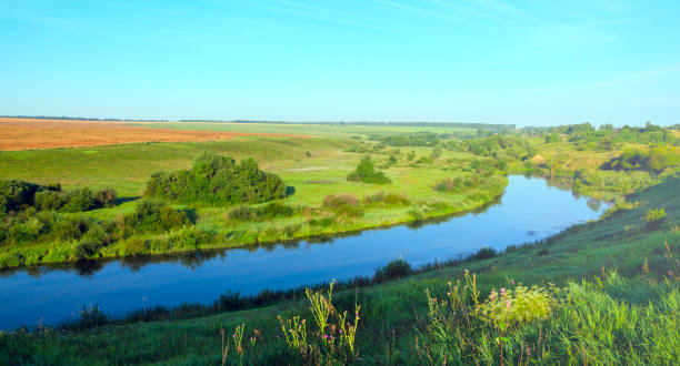 istock Sunny summer landscape.Green hills,fields and meadows.Sunrise.Quiet stream.Calm.Warm sunlight.Cloudless clear bright blue sky. 933789892