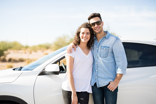 Portrait of beautiful young couple standing together near car outdoors and smiling while on road trip