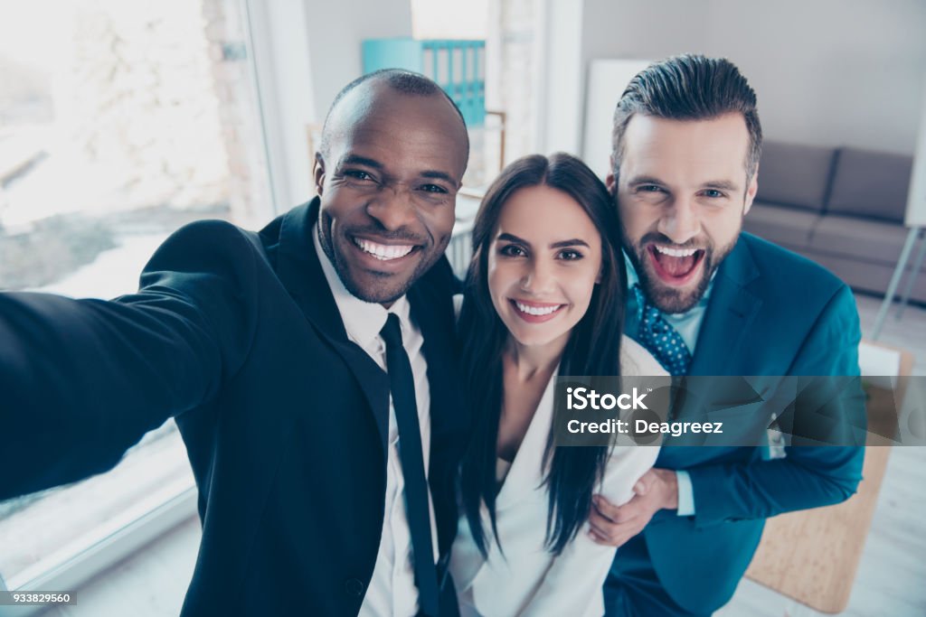 Self portrait of stylish successful, professional trio, afro-american black man with stubble shooting selfie with hand on smart phone with friends, together standing in work place, station Selfie Stock Photo