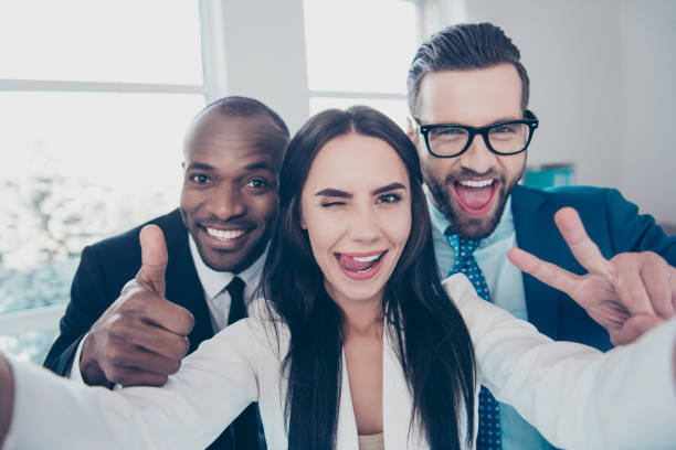 istock Three comic, funny, crazy partners, colleagues having fun, men with bristle showing like symbol and two fingers, peace sign with hands, girl shooting selfie and gesture tongue out, wink with one eye 933838096