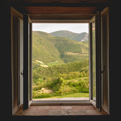 View of a green valley and mountains in the Italian region of Umbria through an open window of a rural building. Square format.