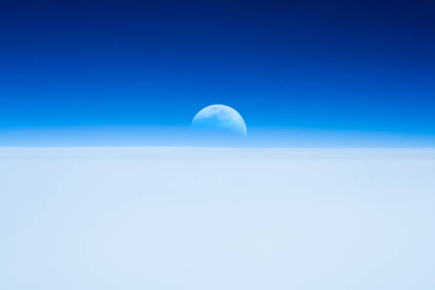Half Moon rising from the Earth horizon above the clouds.