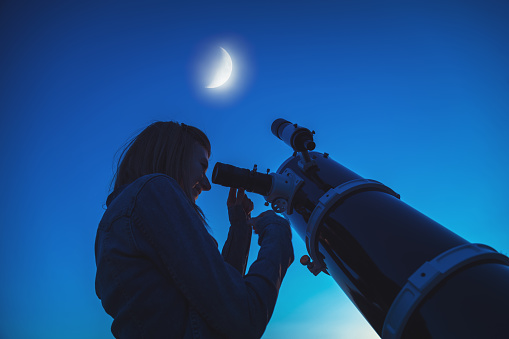 Silhouette of a girl and telescope with Moon on the sky. My astronomy work.