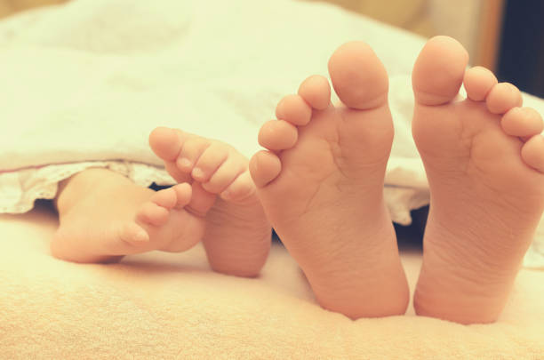 istock Baby feet from under the blanket on the bed. 933850330