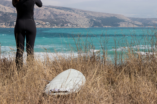 Surfboard in grass with woman in wetsuit standing in the back