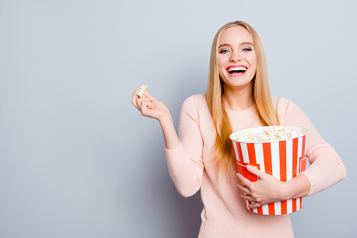 Portrait of charming lovely cute relaxed carefree delightful rejoicing beautiful with long blond hair toothy beaming smile teen age girl watching movie at home eating popcorn isolated gray background