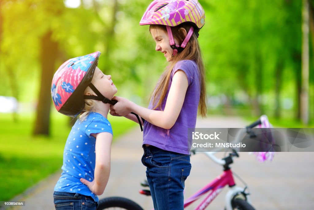 Adorable girl helping her sister to put a bicycle helmet on Adorable girl helping her little sister to put a bicycle helmet on Child Stock Photo