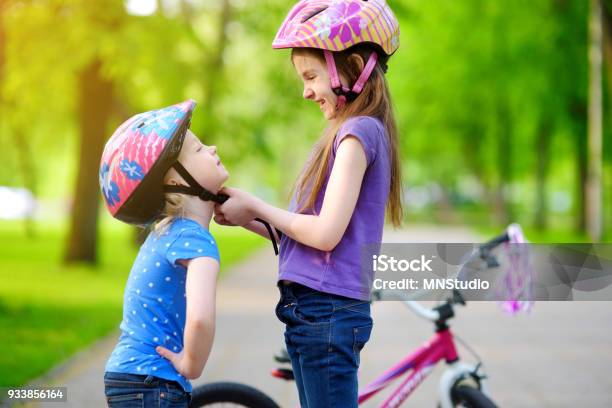 Adorable Girl Helping Her Sister To Put A Bicycle Helmet On Stock Photo - Download Image Now