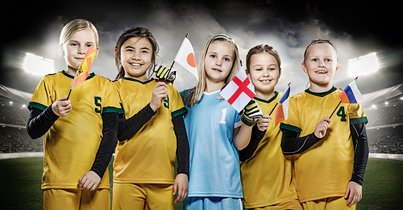 Girls football team holding national flags posing for soccer team photo in a floodlit stadium