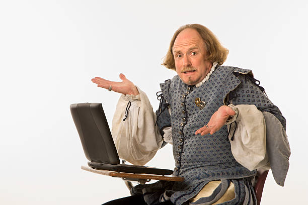 Shakespeare with computer. William Shakespeare in period clothing sitting in school desk with laptop computer shrugging at viewer. shakespeare funny stock pictures, royalty-free photos & images