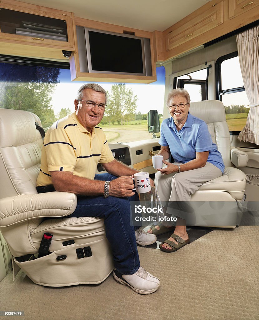 Senior couple sitting in RV. Senior couple sitting in RV holding coffee cups and smiling. Motor Home Stock Photo