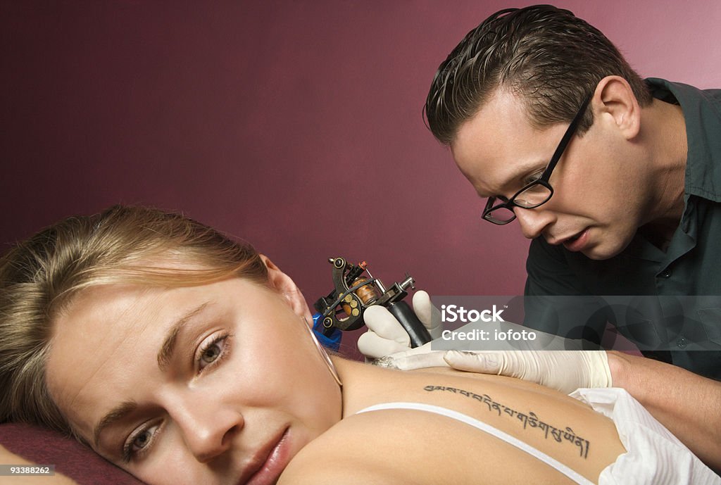 Woman getting tattooed. Caucasian male tattoo artist tattooing Caucasian woman. 25-29 Years Stock Photo