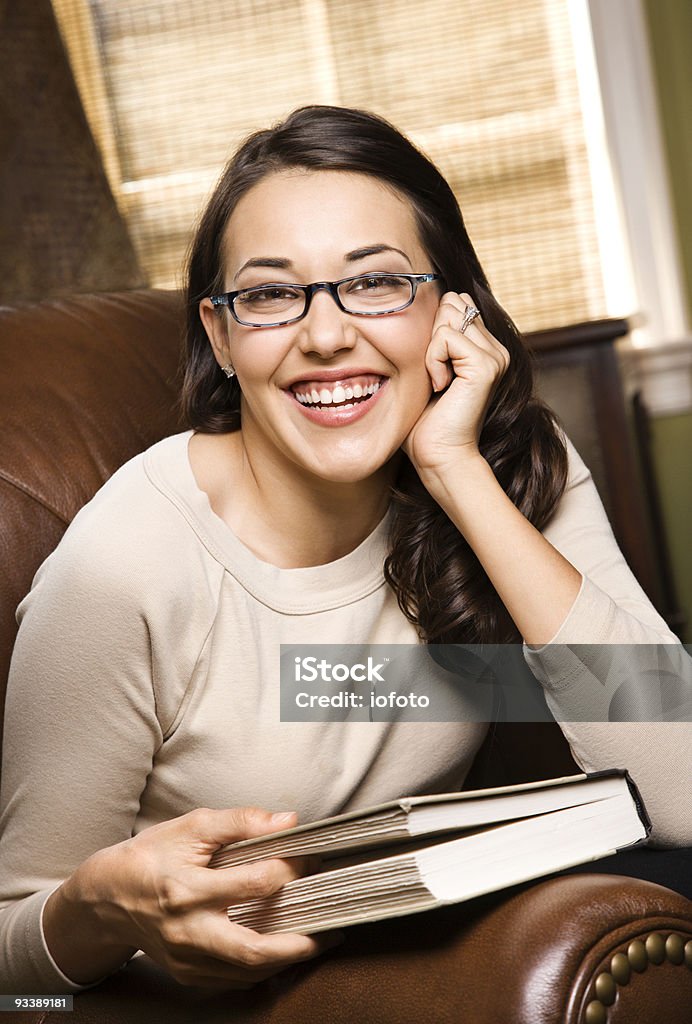 Smiling woman holding a book. Hispanic young woman sitting in leather chair holding a book and smiling at viewer. 20-24 Years Stock Photo