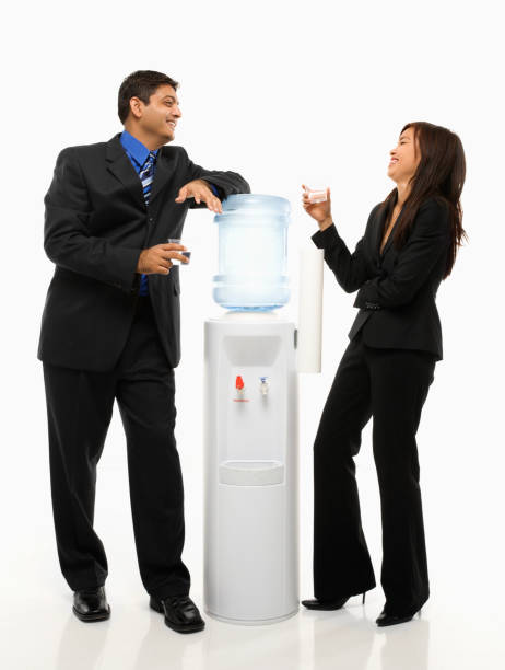 Businessman and businesswoman standing at water cooler. Vietnamese businesswoman and Indian businessman conversing at water cooler. water cooler stock pictures, royalty-free photos & images