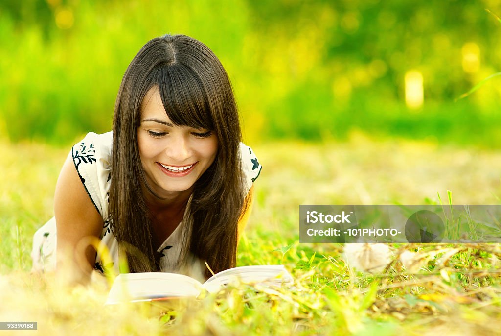 Girl reads book on meadow Young beautiful woman lays on green field and reads book. Adolescence Stock Photo