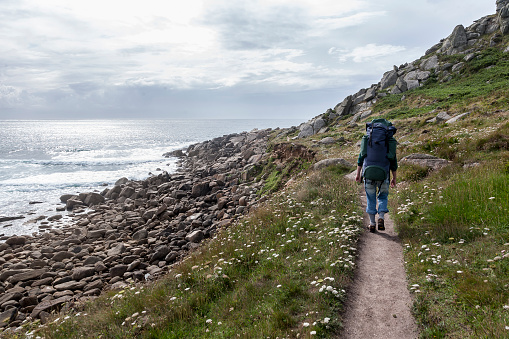 A backpacker on her way in Cornwall hills on the coast by the Celtic Sea