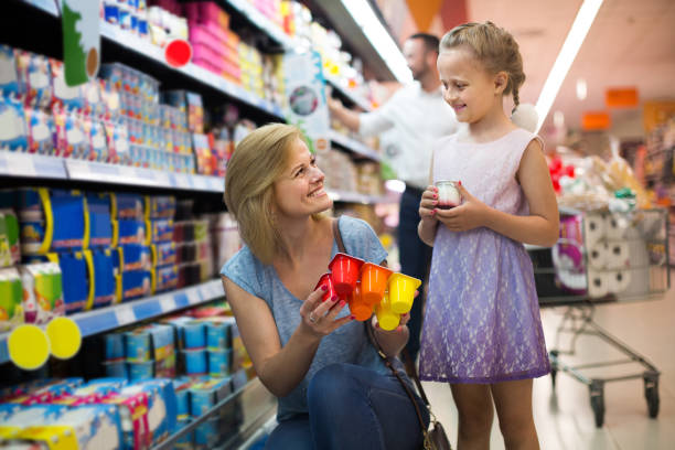 portrait of  woman and girl holding package with yogurt in grocery shop - three different refrigerators imagens e fotografias de stock