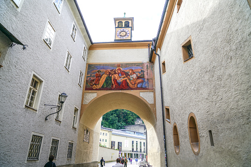 Religious scene of Jesus after crucifixion with Mary and apostles painted above arch and people walking along narrow road between tall traditional buildings in old town  September 6 2017 Salzburg Austria