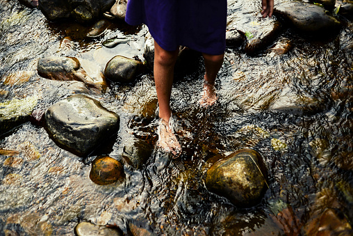 The feet of a child in a river or stream, barefoot and standing on rocks, water is moving slightly