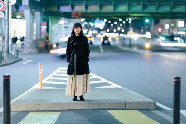 A young Japanese woman is standing alone in the streets at night in Ginza, Tokyo.