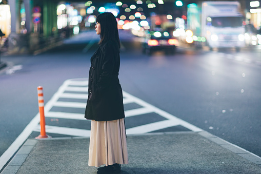 A young Japanese woman is standing alone in the streets at night in Ginza, Tokyo.