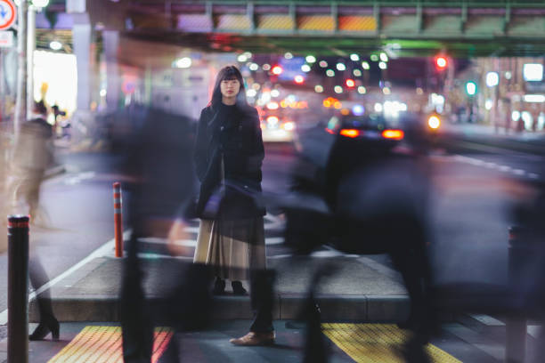 Woman standing in the street at night in Tokyo A young woman standing in the street at night in Ginza, Tokyo. long exposure stock pictures, royalty-free photos & images