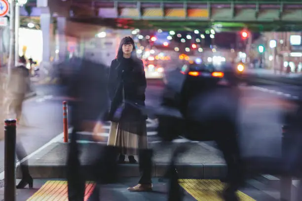 A young woman standing in the street at night in Ginza, Tokyo.